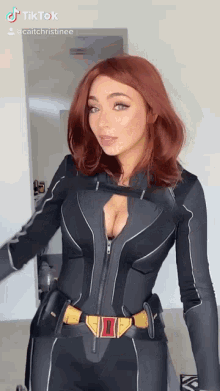 a woman with red hair is wearing a black suit with a plunging neckline and a gold belt .