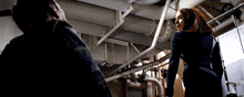 a man and woman are standing in a dark room with pipes