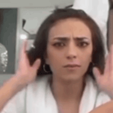 a woman in a white robe is making a funny face with her hands on her ears .