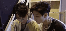 two young men are standing next to each other in a room and looking at something .