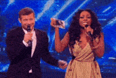 a man in a suit holds a microphone next to a woman in a gold dress