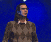 a man wearing glasses and a plaid sweater stands in front of a blue background that says you