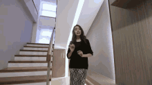 a woman in a black top and striped pants is standing in front of a set of stairs