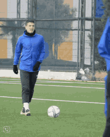 a man in a blue jacket kicks a soccer ball on a soccer field