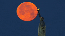 a plane is flying over the statue of liberty with a full moon in the background