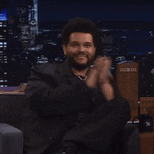 a man in a black suit is clapping his hands in front of a city skyline