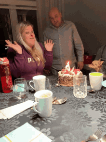 a woman stands in front of a birthday cake with a candle lit up