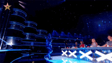 a man in a mask stands on a stage in front of a judge 's table that says " xxx "