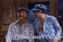 two men in blue hats are standing next to each other in a living room and laughing .