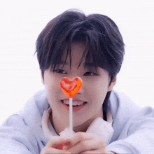 a young man is holding a heart shaped lollipop in his hand .