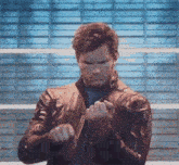 a man in a leather jacket is standing in front of a brick wall and making a funny face .