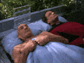 two men are laying on a bed with a blue blanket