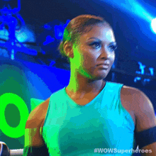 a woman in a blue tank top is standing in front of a green sign that says wowsuperheroes .