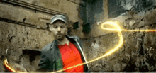 a man in a red shirt is standing in front of a brick wall with a light trail behind him