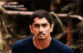 a man in a blue shirt is standing in front of a blurred background .
