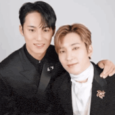 two men in suits are posing for a picture and one has a brooch on his lapel
