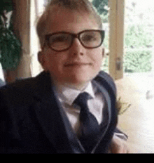 a young boy wearing glasses and a suit and tie is smiling .