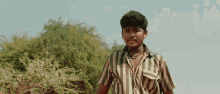 a boy wearing a striped shirt stands in front of a tree