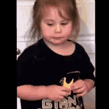a little girl wearing a black shirt is eating a banana .
