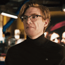 a man wearing glasses and a black turtleneck sweater makes a funny face