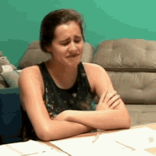 a woman is crying while sitting at a table with her arms crossed and a couch in the background .