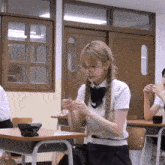 a girl wearing glasses sits at a desk in a school classroom