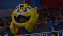 a yellow cat mascot with a soccer ball in his mouth