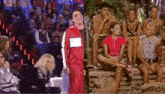 a man in a red jacket is standing next to a group of people sitting on a wooden pallet .