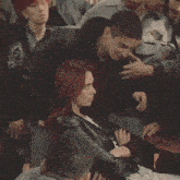a woman with red hair is sitting in a crowd while a man holds her arm