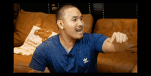 a man wearing a blue adidas shirt sitting on a couch