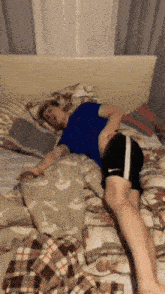 a man laying on a bed with a blue shirt and black shorts