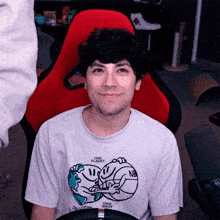 a man wearing a one planet t-shirt smiles while sitting in a red chair