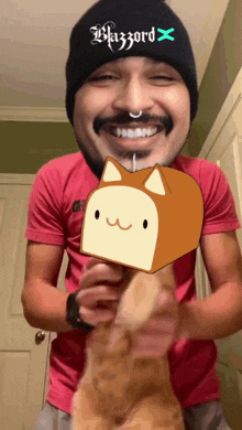 a man wearing a beanie that says blizzard x holds a cat