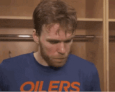 a man wearing a blue oilers shirt is standing in a locker room .