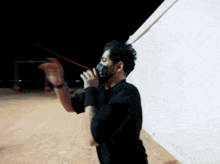 a man wearing a mask is standing in front of a wall at night