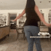 a woman is dancing in a living room in front of a table and chairs .