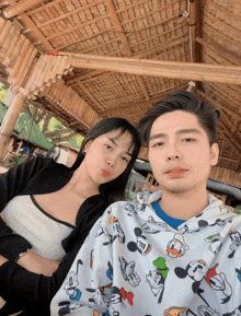 a man and a woman pose for a picture under a thatched hut