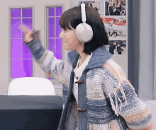 a woman wearing a sweater and headphones is waving her hand