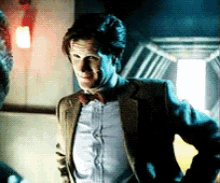 a man in a suit and bow tie stands in a dark room with his hands on his hips