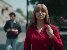a woman in a red shirt is walking down the street with a man in a black jacket behind her