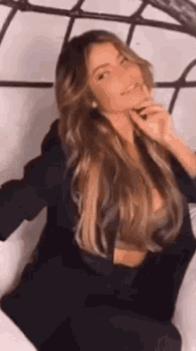 a woman with long hair is sitting on a bed with her hand on her chin .