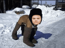 a young boy wearing a hat and boots is standing in the snow