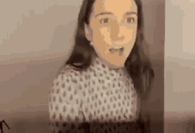 a woman in a polka dot shirt is standing in front of a wall and making a funny face .