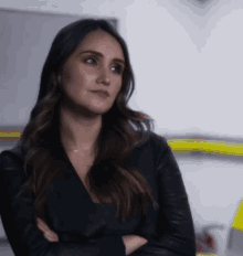 a woman in a black jacket with her arms crossed looks to the side