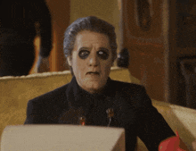 a man with black paint on his eyes is sitting on a couch looking at something