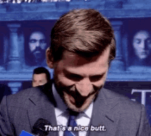 a man in a suit and tie is talking into a microphone and says that 's a nice butt