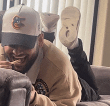 a man wearing an orioles hat is laying on a couch with his feet up