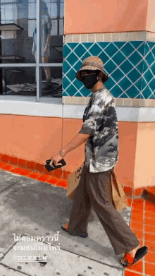 a man wearing a hat and a mask is walking on the sidewalk