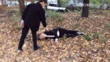 a man standing next to a person laying on the ground in the woods