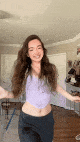 a young woman in a purple top and black pants is dancing in a room